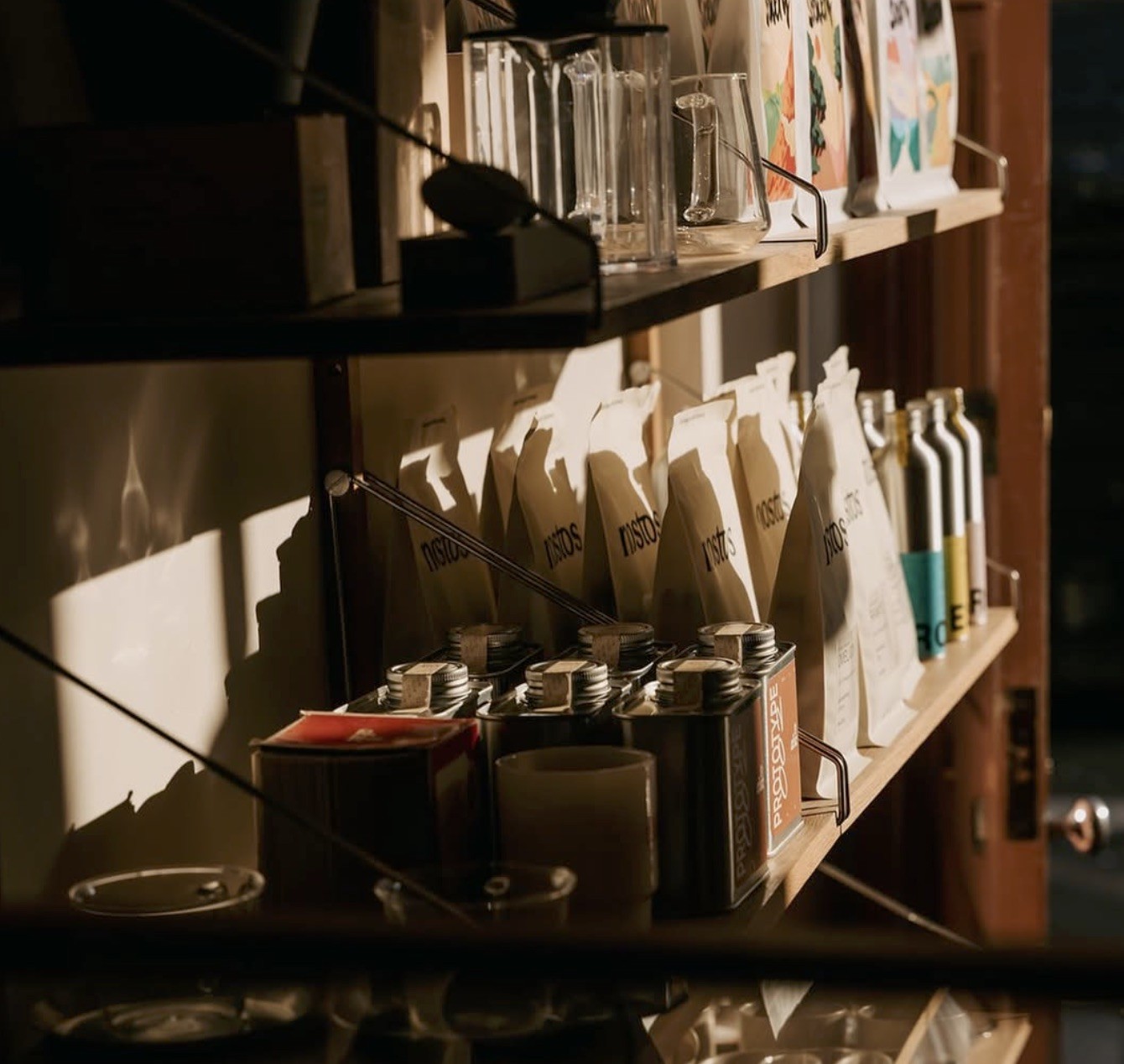 Retail coffee bags and small tinned goods lit by afternoon sun on wooden shelving at LOAM