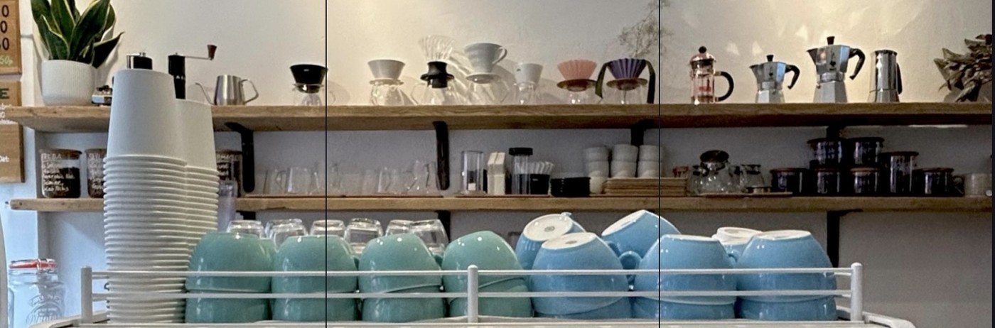 Open wooden shelves stocked with pourover drippers, moka pots, and stacked pastel mugs at Triple Point Coffee