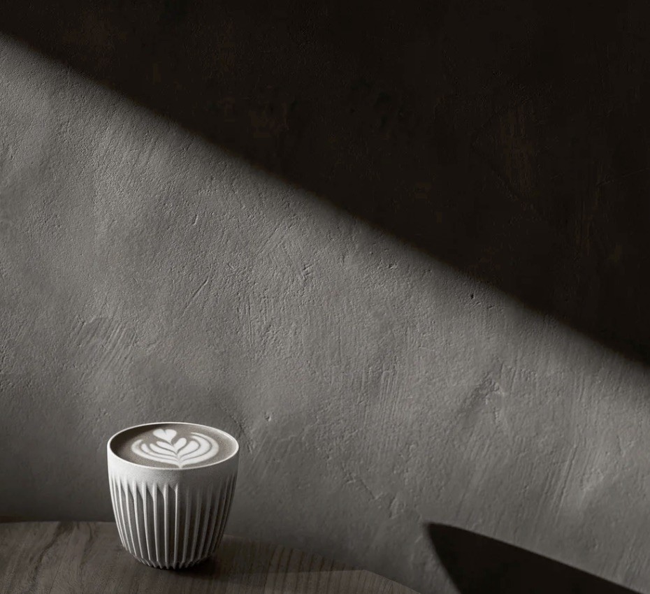 A ribbed ceramic cup of latte art lit by a diagonal beam of light against a raw plaster wall at WOLFOX