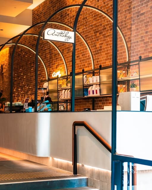 The arched brick counter and neon-lit shelving at Coffee Anthology, with a barista in motion behind the bar