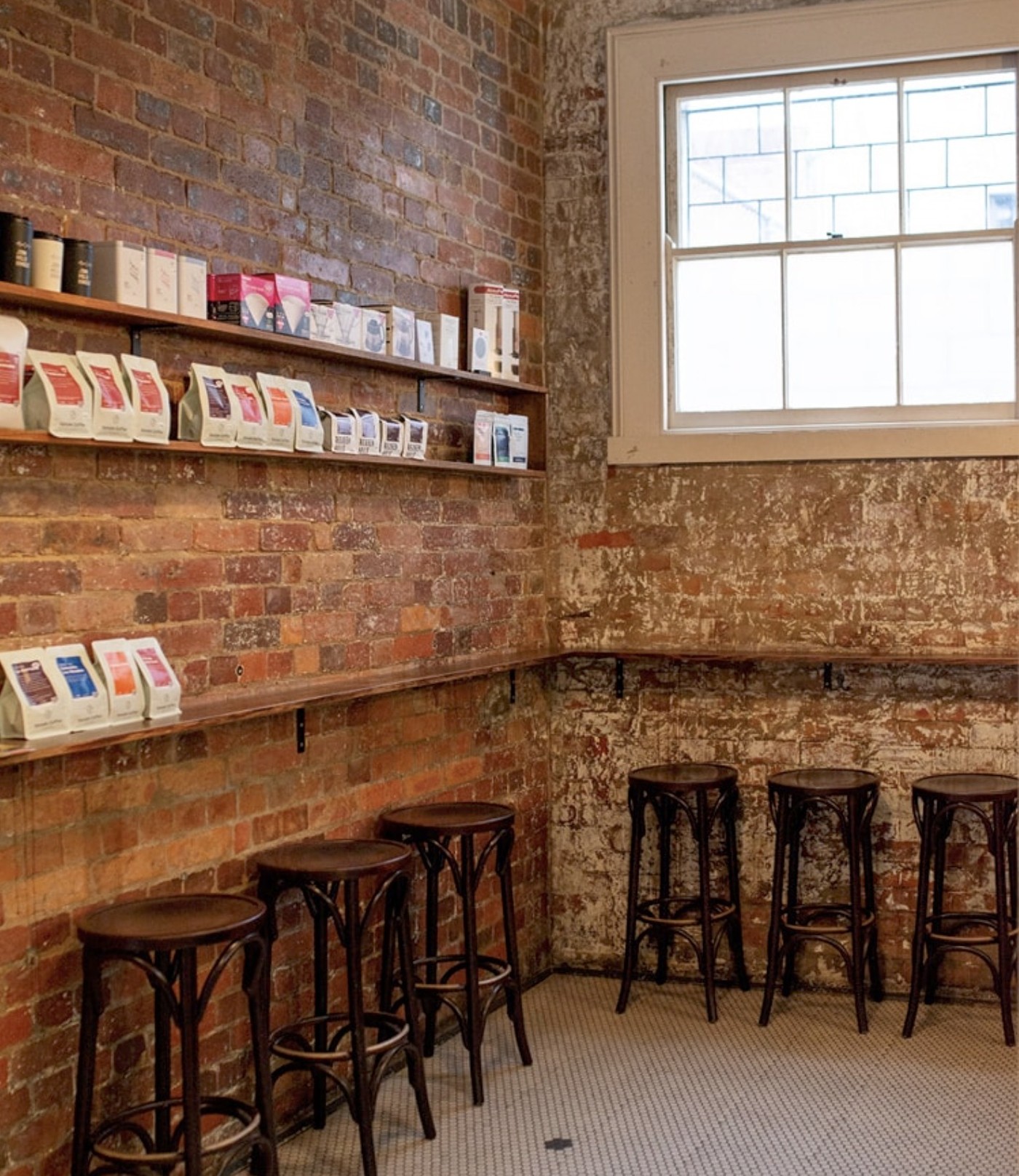 Bare brick walls lined with shelves of retail bean bags and pour over gear, bentwood bar stools along the penny tiled floor at John Mills Himself