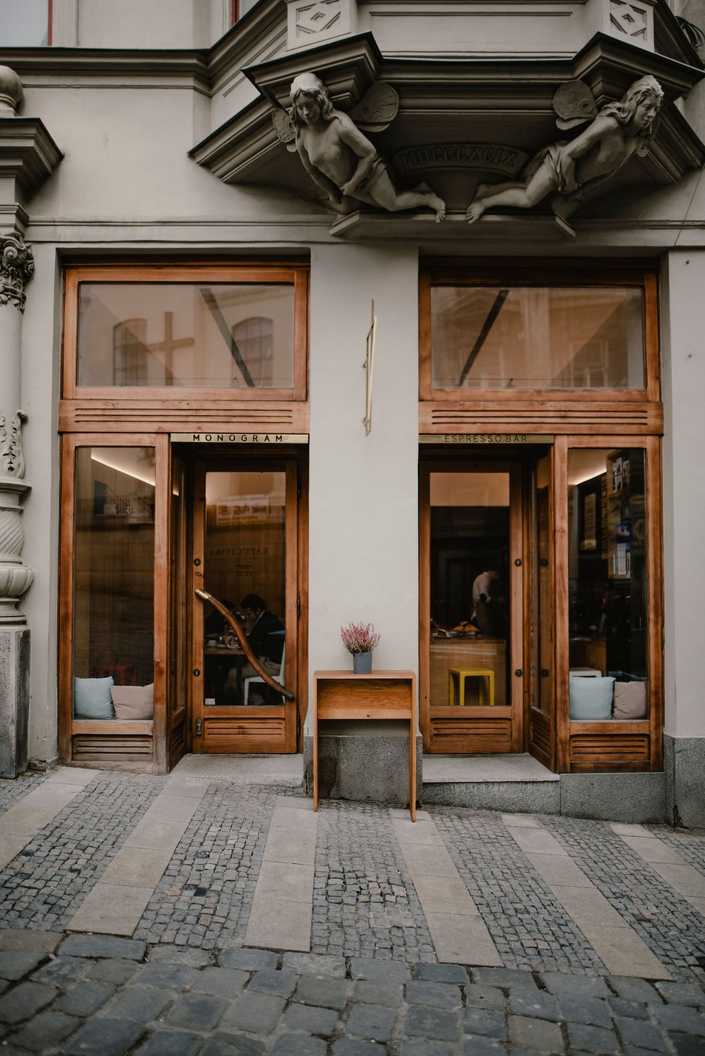 The wooden double storefront of Monogram Espresso Bar beneath ornate carved figures on the building facade