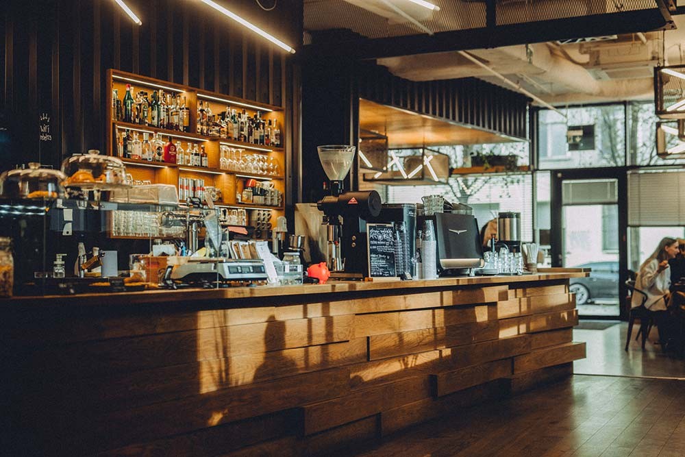 A warm wood bar counter with a espresso machine and shelves of bottles at Rebelbean Vlněna