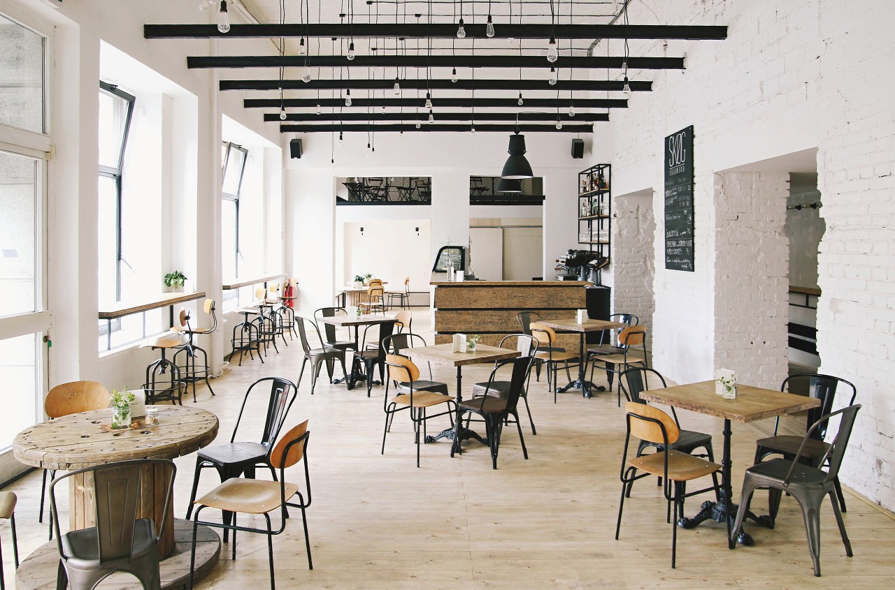 The bright, high ceilinged main room at SKØG Urban Hub with wooden tables under exposed black beam lighting