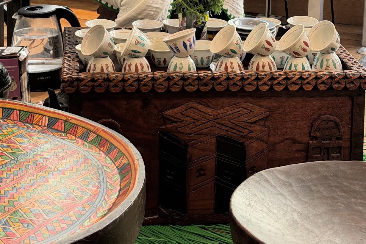 A carved wooden chest holding stacked Ethiopian coffee ceremony cups beside a hand painted wooden tray at Addis Stories