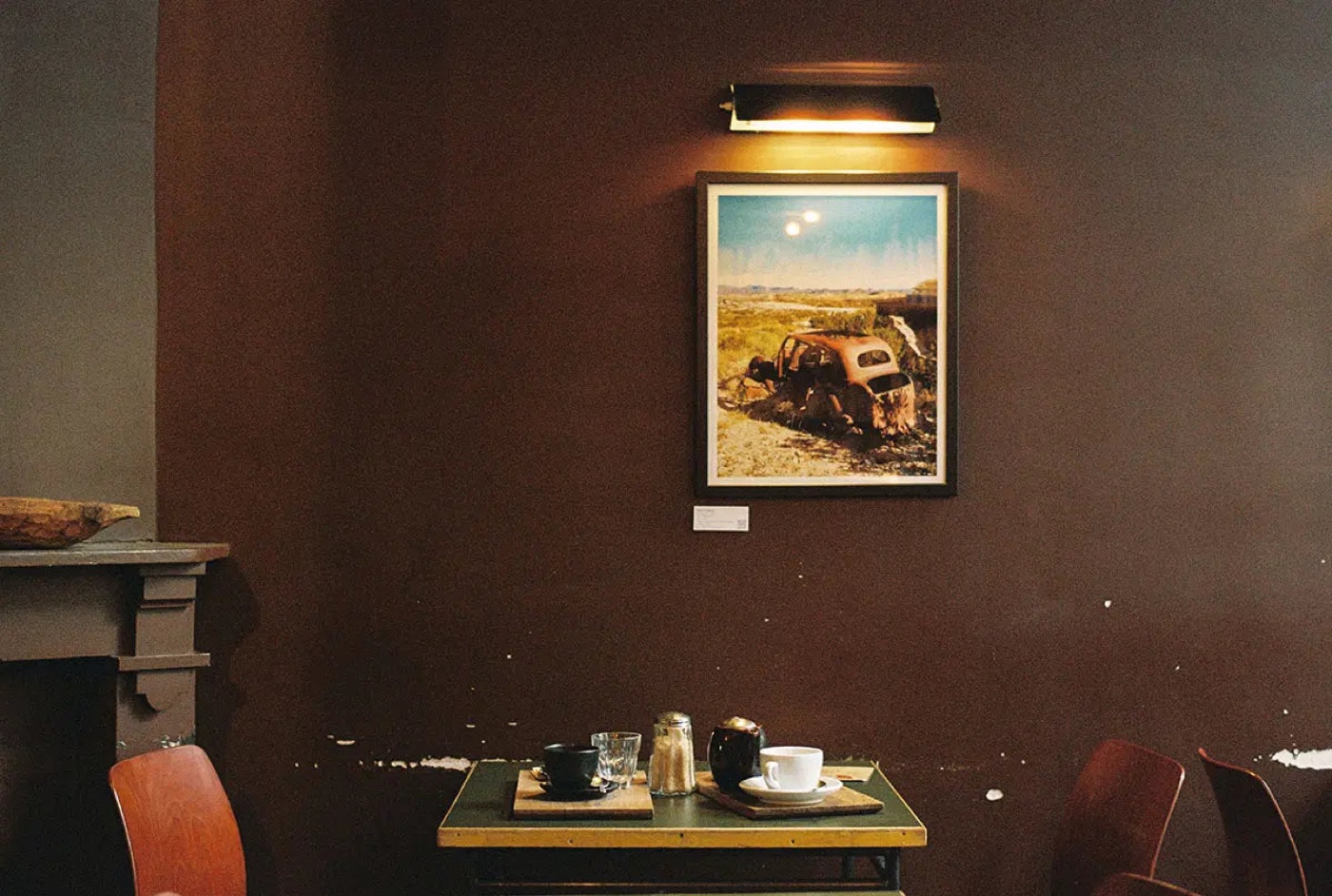 A cafe table set beneath a framed photograph on a dark painted wall at the Belga & Co Bailli shop