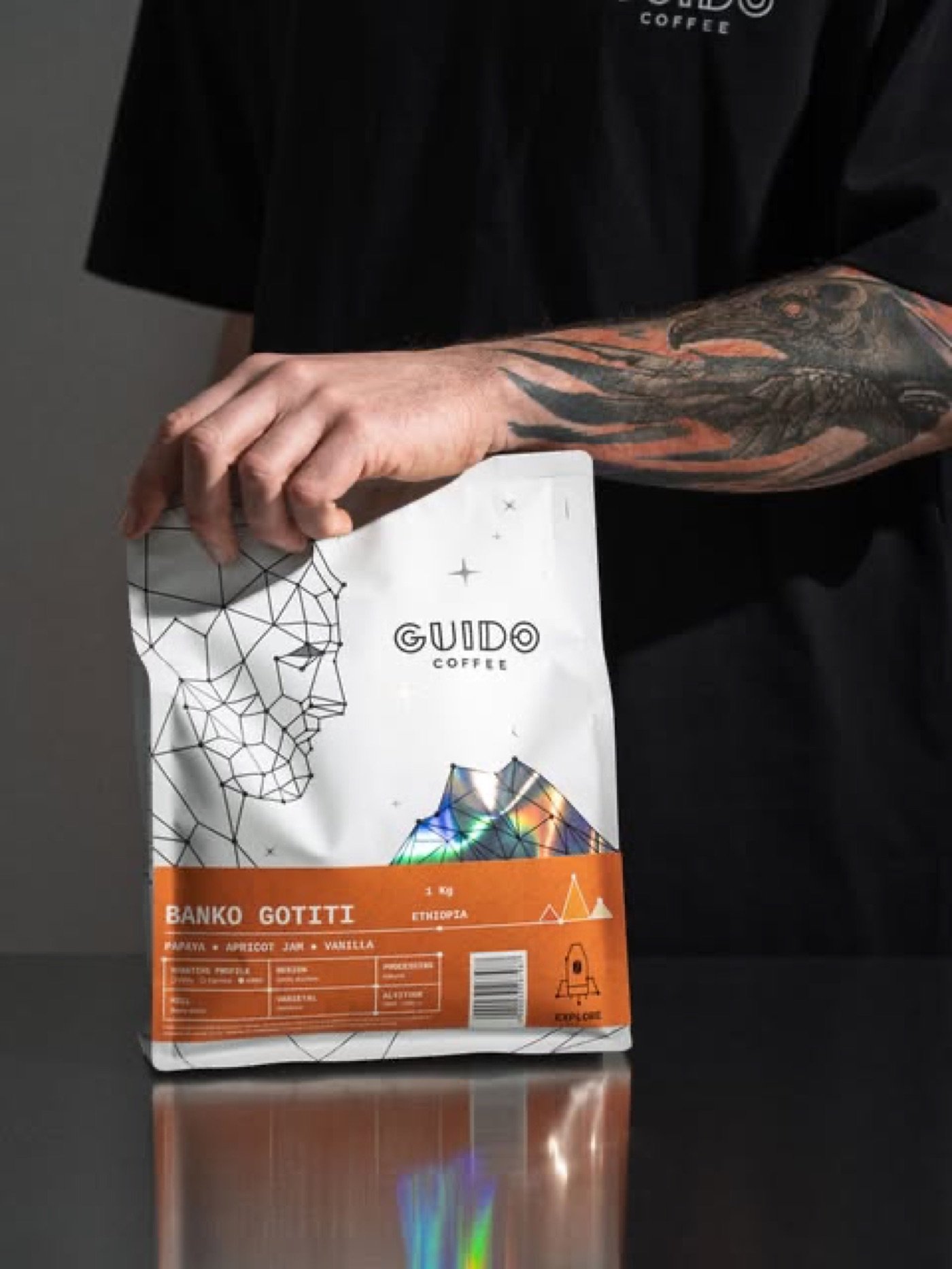A hand holding a bag of Guido Coffee retail beans