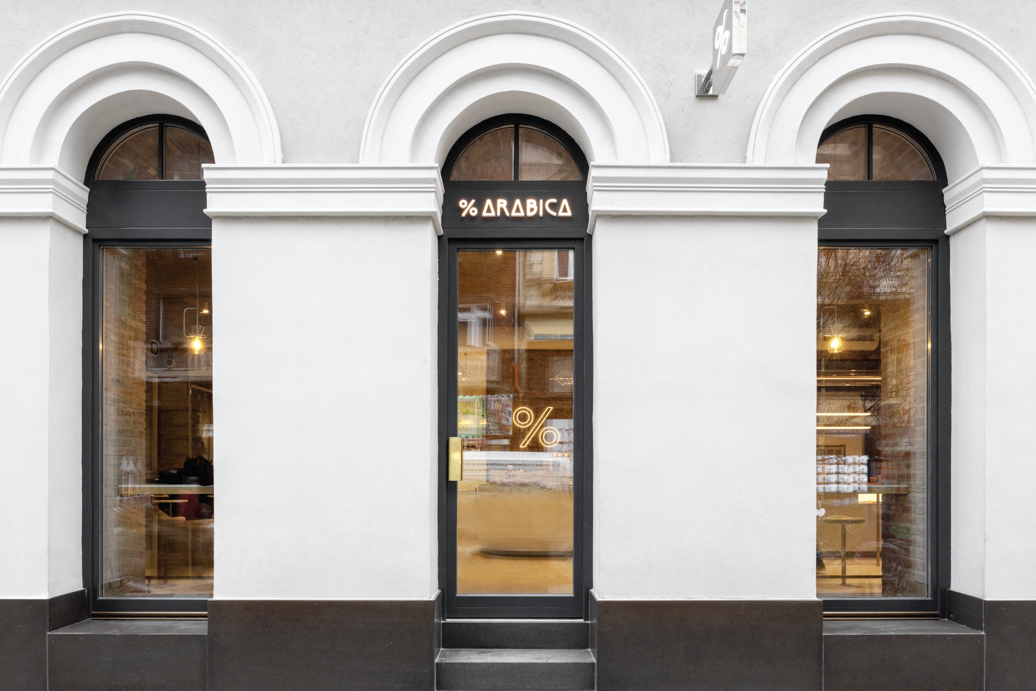The arched 1844 facade of % Arabica Budapest Király on Király utca, the lit % Arabica sign above the doorway