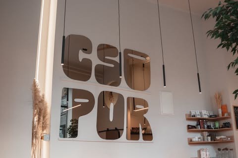 The mirrored CSUPOR wordmark on the wall at Csupor, hanging pendant lights and a retail shelf beneath