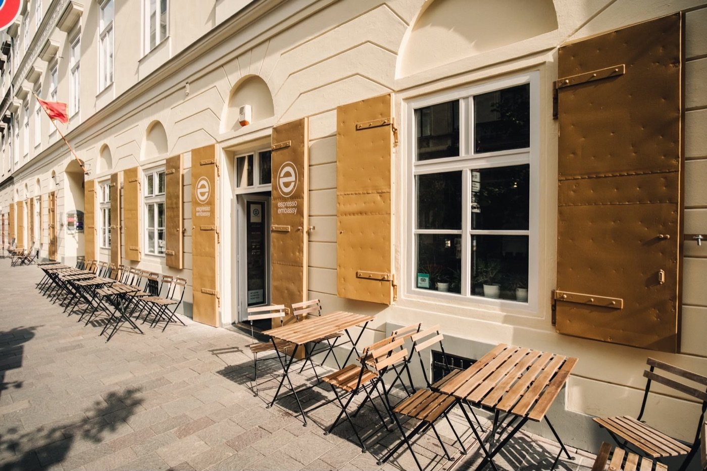 The Espresso Embassy storefront with gold shutters open and outdoor tables set along the sidewalk