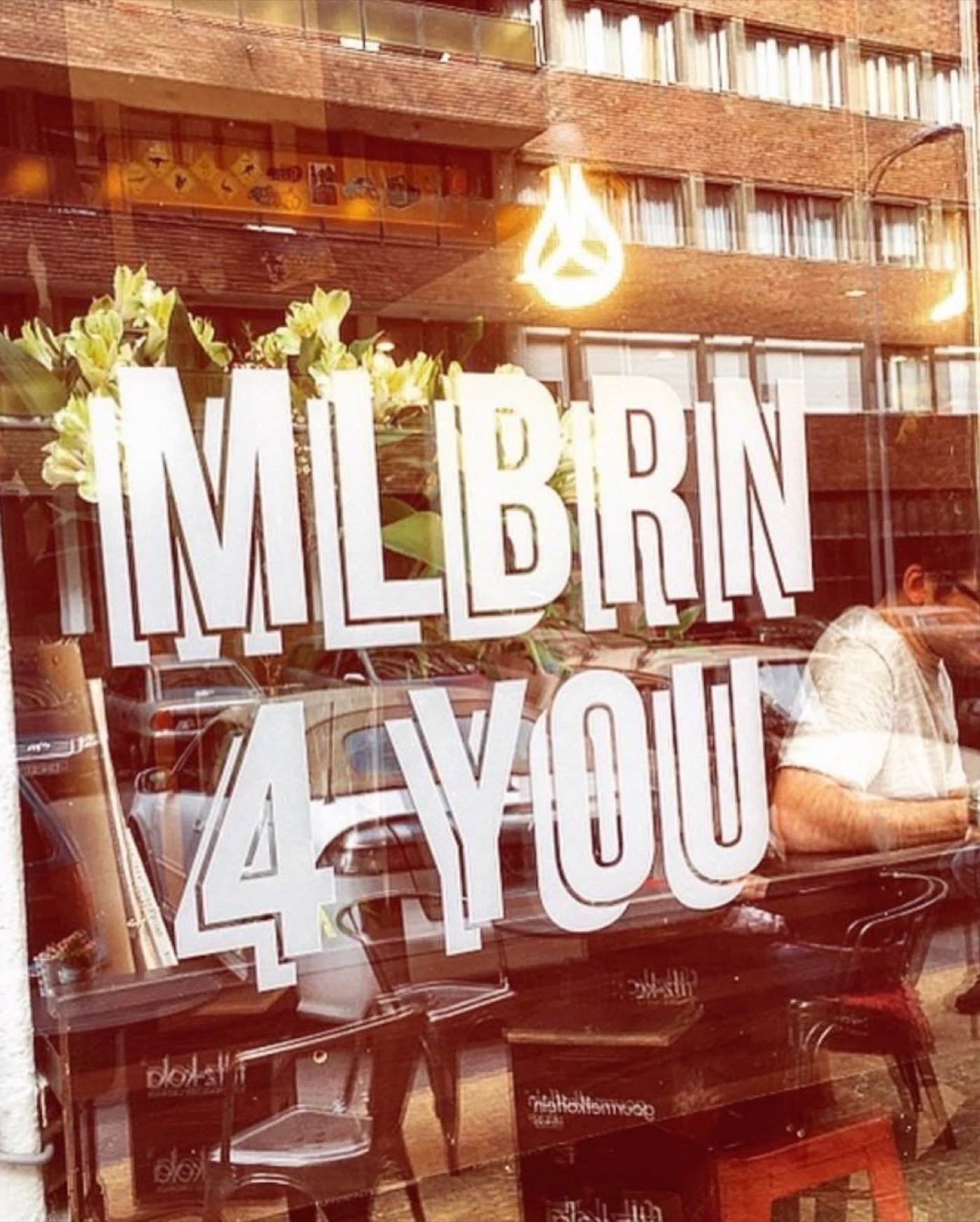 The window lettering at My Little Melbourne, 'MLBRN 4 YOU,' with flowers tucked above the glass