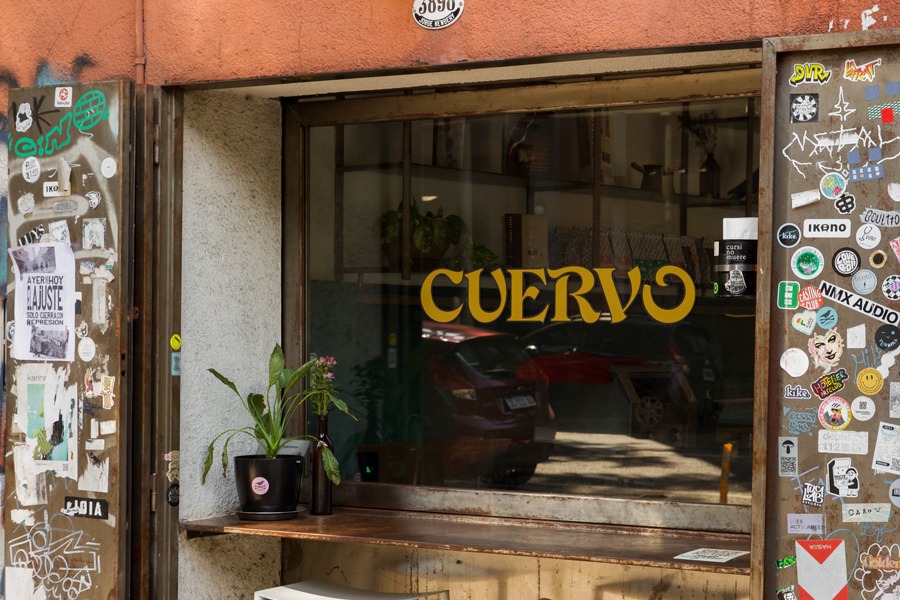 Cuervo's Chacarita storefront on Jorge Newbery, a gold CUERVO sign painted on the street window above a wooden counter, framed by sticker covered steel shutters