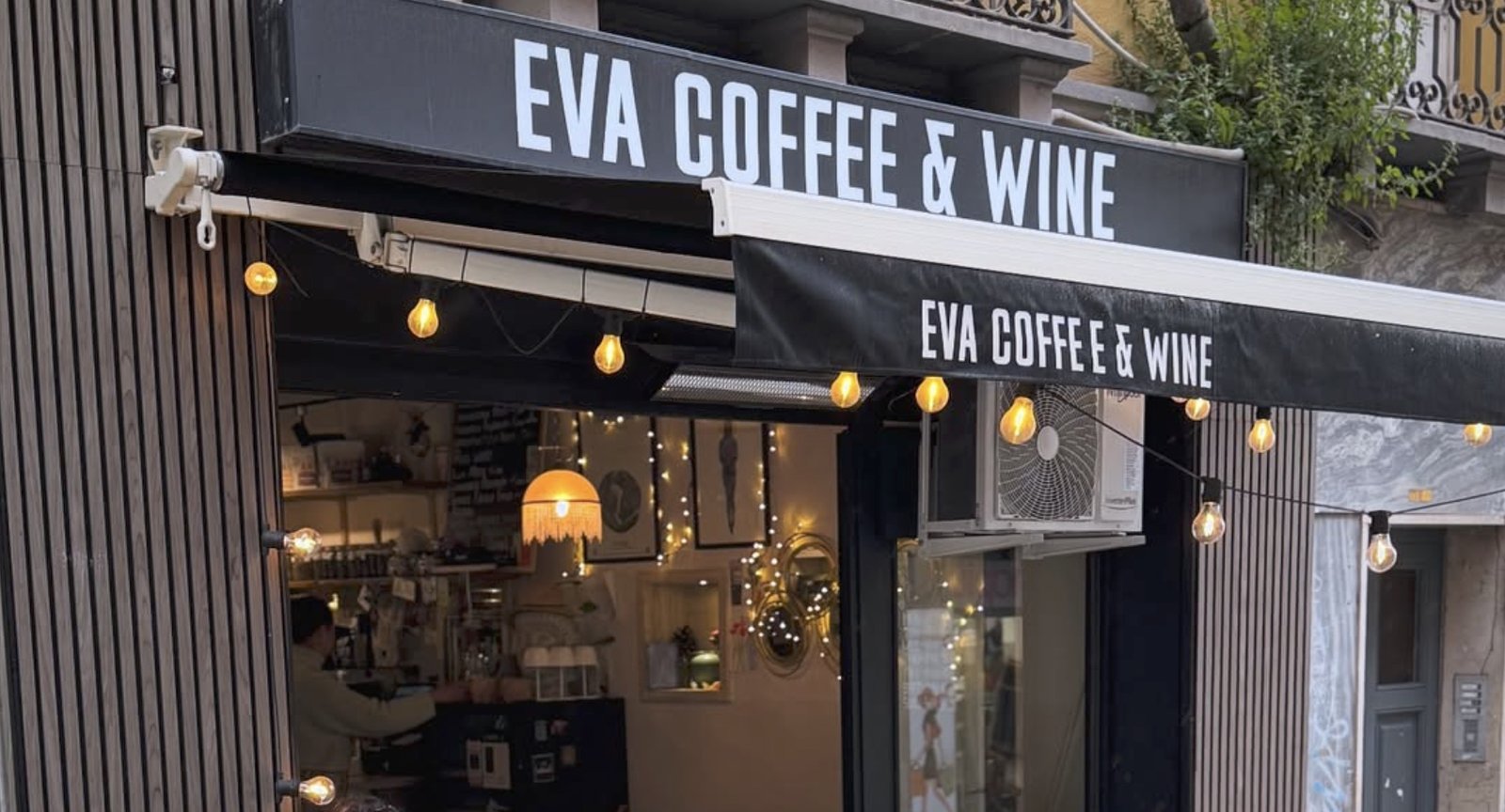 The storefront awning of EVA Coffee & Wine, strung with string lights, with the counter visible through the open window