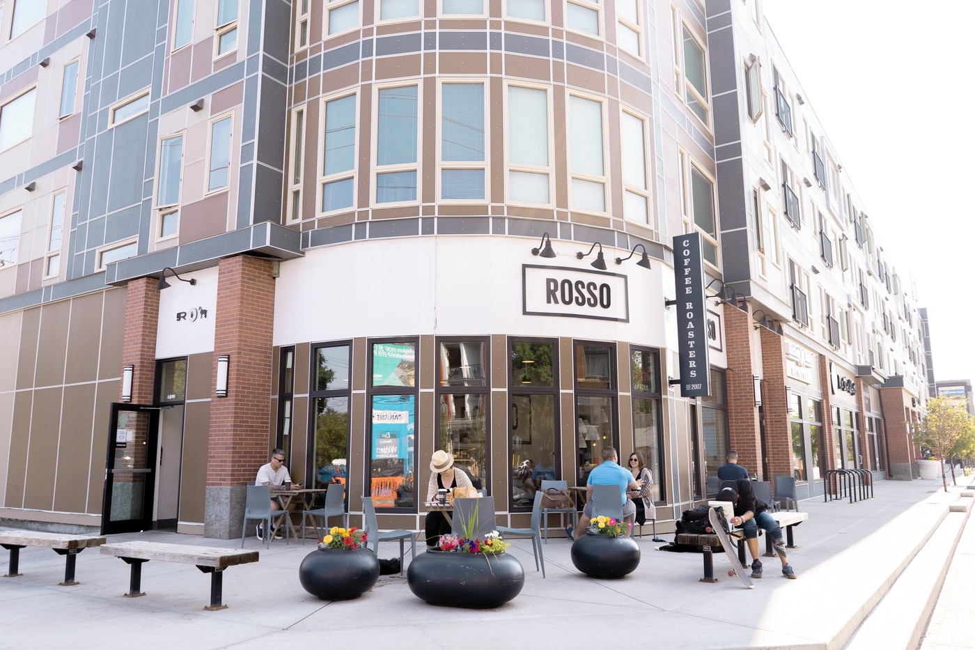The corner storefront on 9th Avenue with a ROSSO Coffee Roasters sign above the entrance and patio tables where a few distant customers sit outside