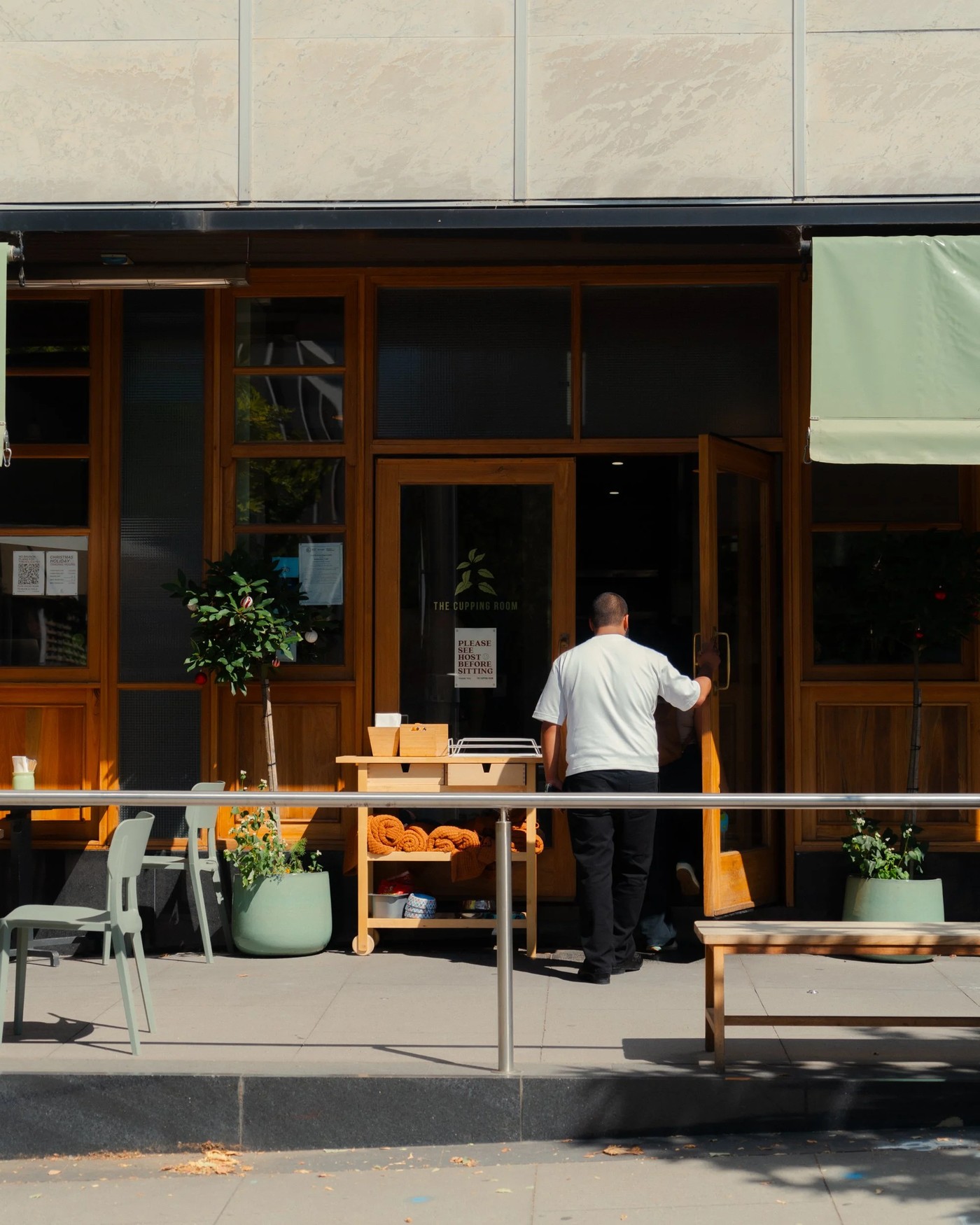 Storefront of The Cupping Room on University Avenue, timber framed windows and door with the shop name lettered on the glass, a staff member back-turned holding the door open