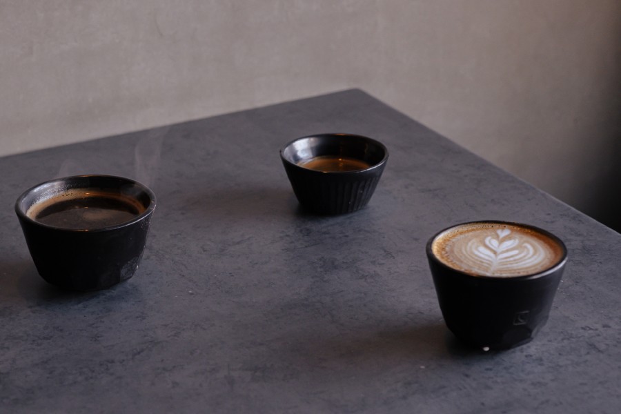 Three small cups of coffee, including one with latte art, sitting on a dark grey concrete table at Intra PRVN