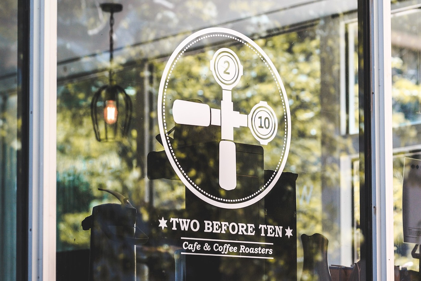 Window decal at Two Before Ten showing the cafe's coffee-plunger logo and the words Two Before Ten, Cafe and Coffee Roasters