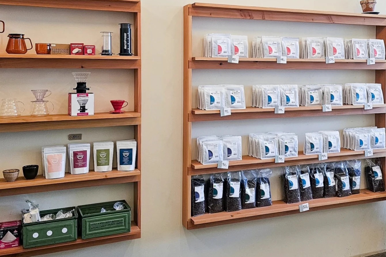 Kontra Coffee's retail wall, shelves of brewing gear like AeroPress and V60 drippers beside rows of priced retail bean bags
