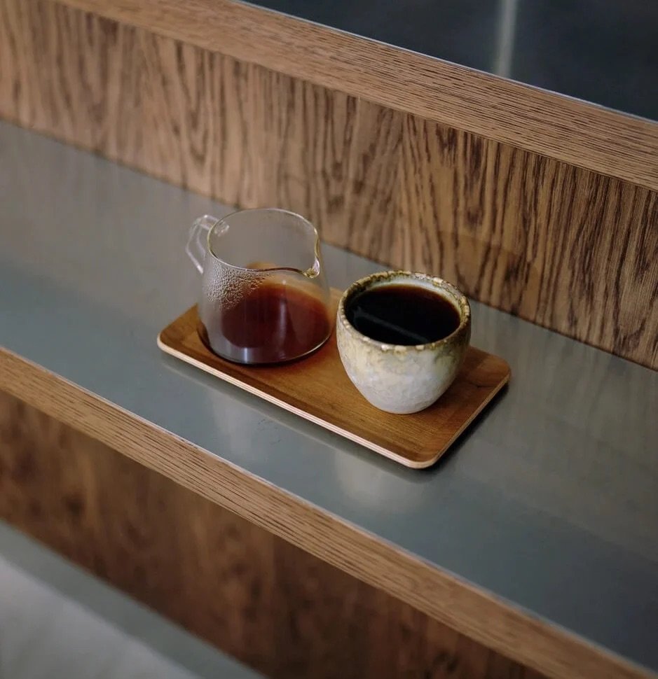 A filter coffee carafe and cup on a wooden tray, set on La Cabra's steel and oak counter