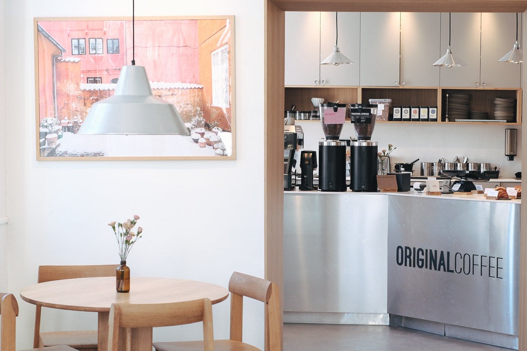 The Original Coffee counter at the Christianshavn shop, with grinders, bean canisters, and a framed photograph on the wall beside a cafe table