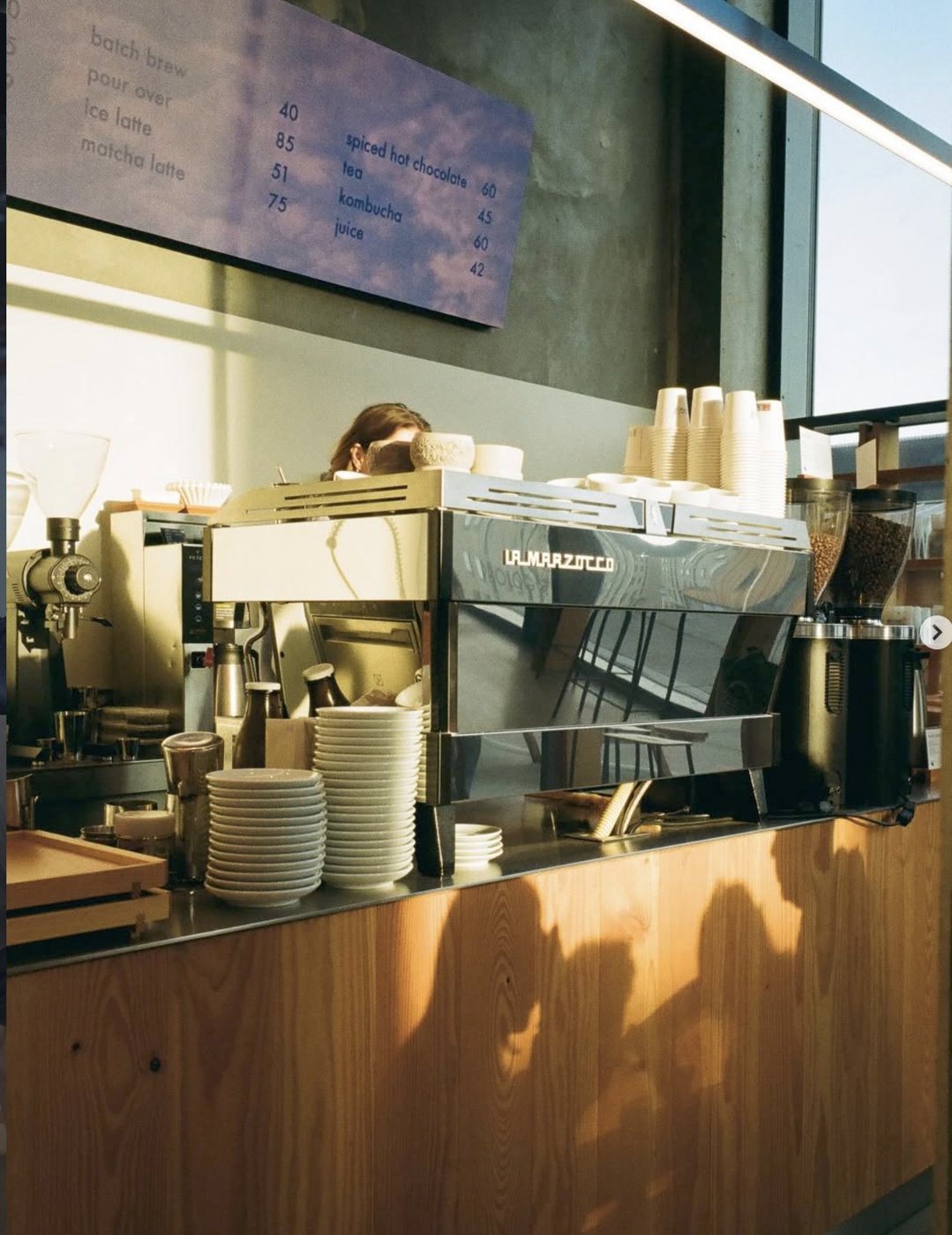 The La Marzocco espresso bar at Prolog Coffee, menu board above, warm afternoon light across the wooden counter