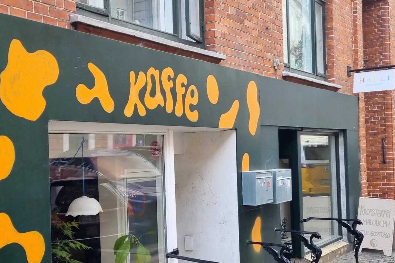 The dark green Saftig storefront in Nørrebro, a hand-painted orange 'kaffe' mural above the entrance