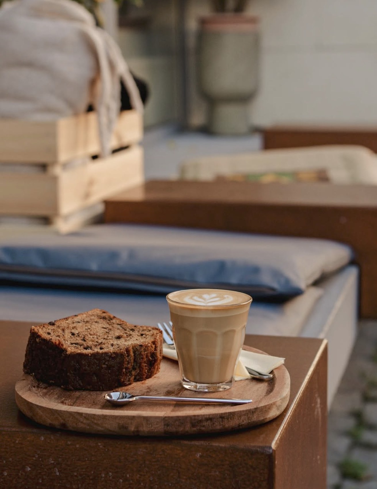 A latte with leaf latte art next to a slice of banana bread on a wooden board at Ganba Coffee