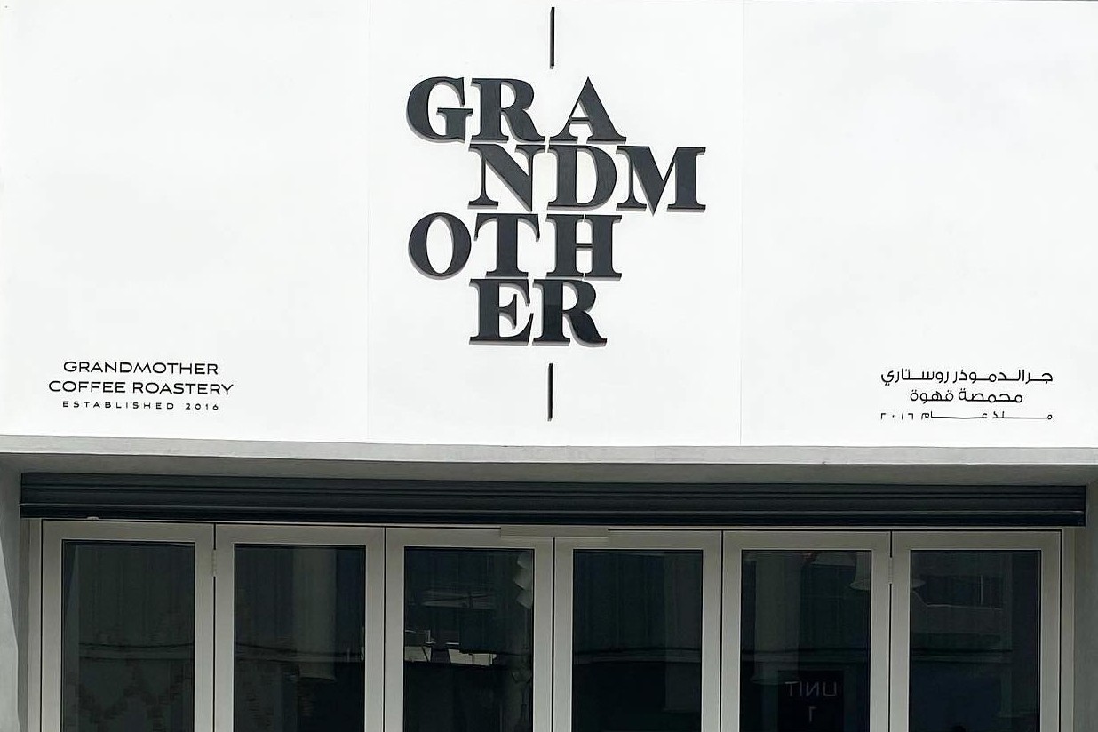 The white storefront of Grandmother Coffee Roastery with its stacked black lettering, Established 2016 in English and Arabic, above folding glass doors