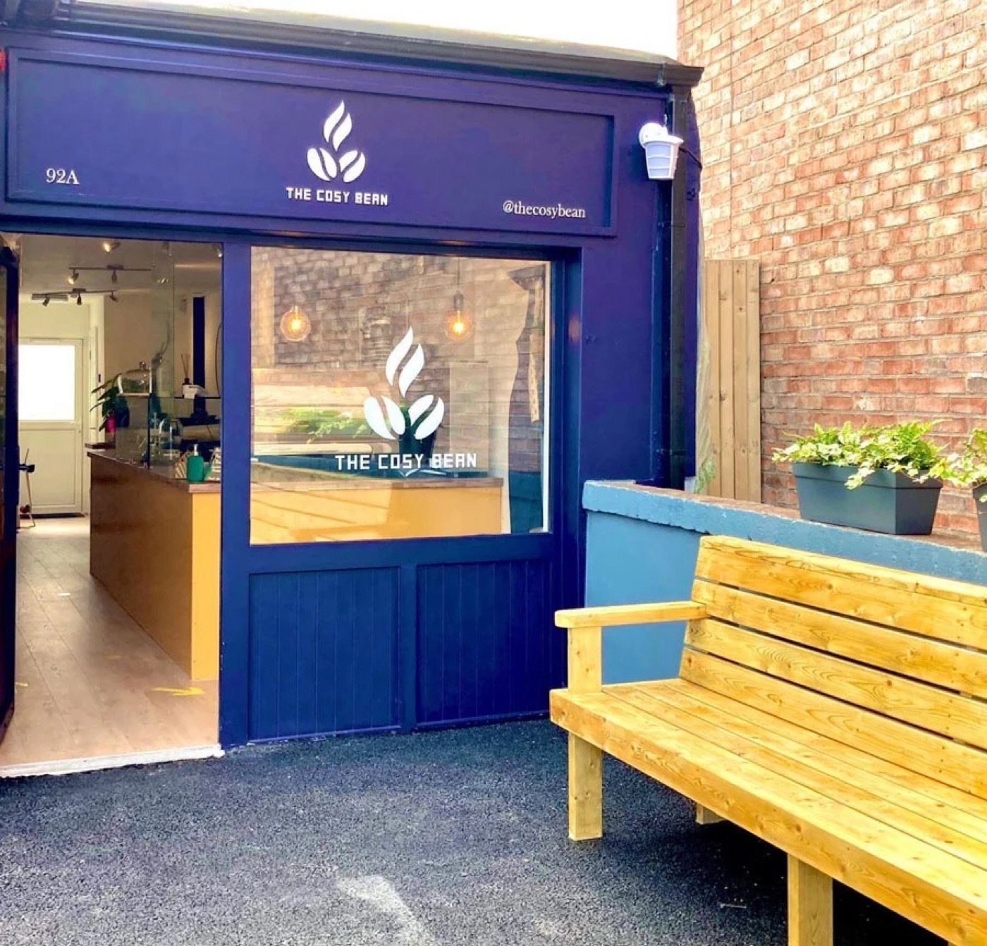 The navy storefront of The Cosy Bean, a wooden bench and potted plants out front