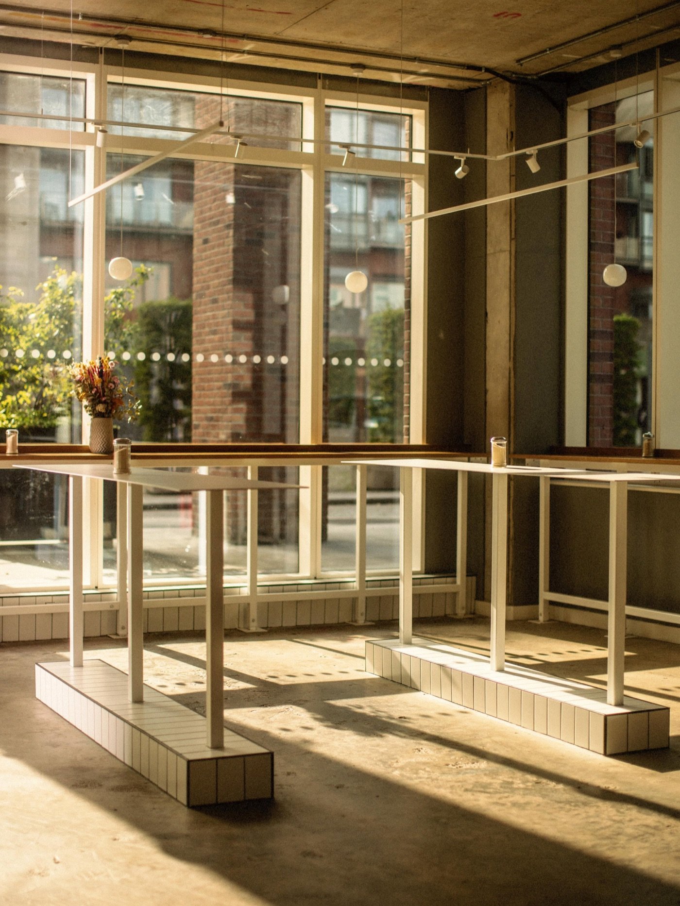 Sunlit standing tables on tiled plinths in front of large windows at Proper Order Coffee Co