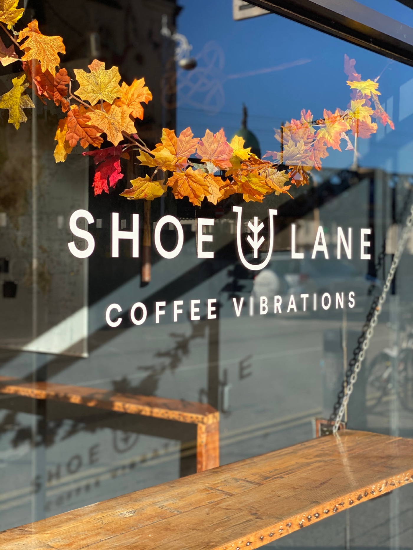 The Shoe Lane Coffee window decal reading 'Coffee Vibrations', autumn leaf garland draped above a wooden bench