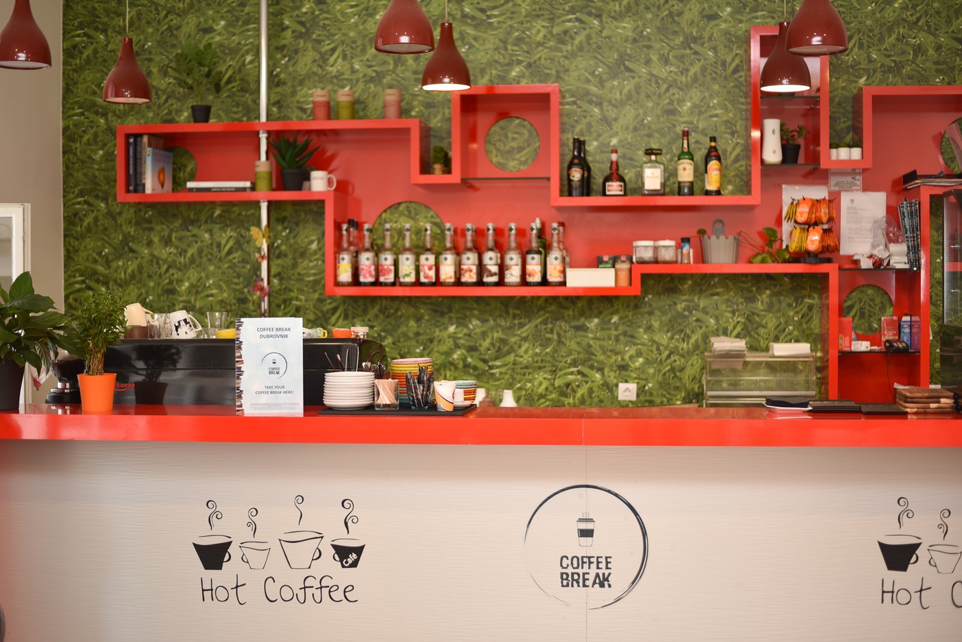 The red counter and green wall shelving inside Coffee Break, with a sign reading Coffee Break Dubrovnik on the bar