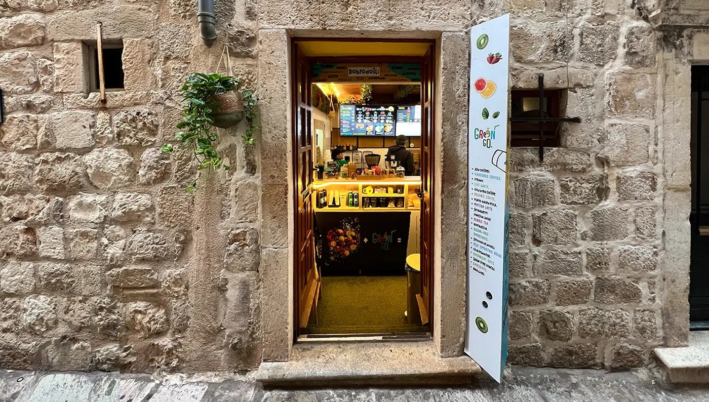 The narrow stone doorway of GreenGo in Dubrovnik's Old Town, open to reveal the counter, menu board and hanging plant