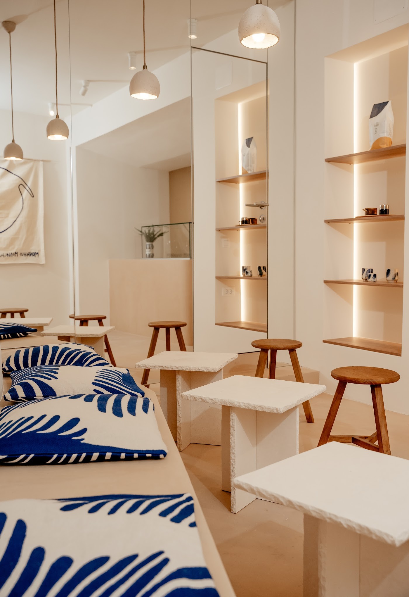 The warm wood and cream interior of Monachus Monachus, with blue patterned cushions, wooden stools and bagged coffee beans on lit shelving