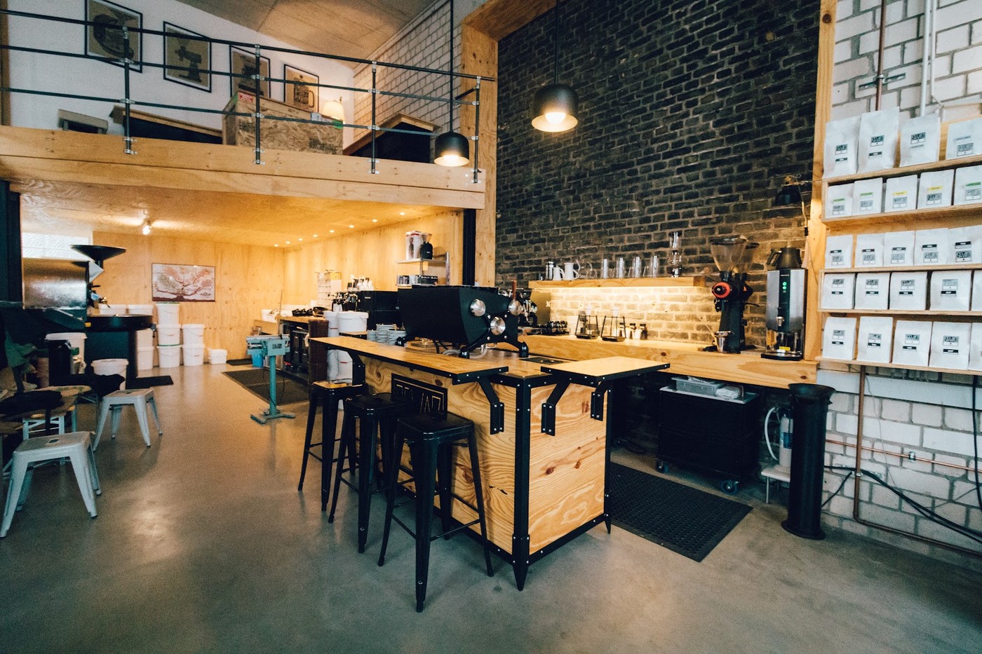 The Schvarz Kaffee cafe interior with a mezzanine loft over a wooden espresso bar, an exposed dark brick wall, and shelves stacked with bags of roasted coffee