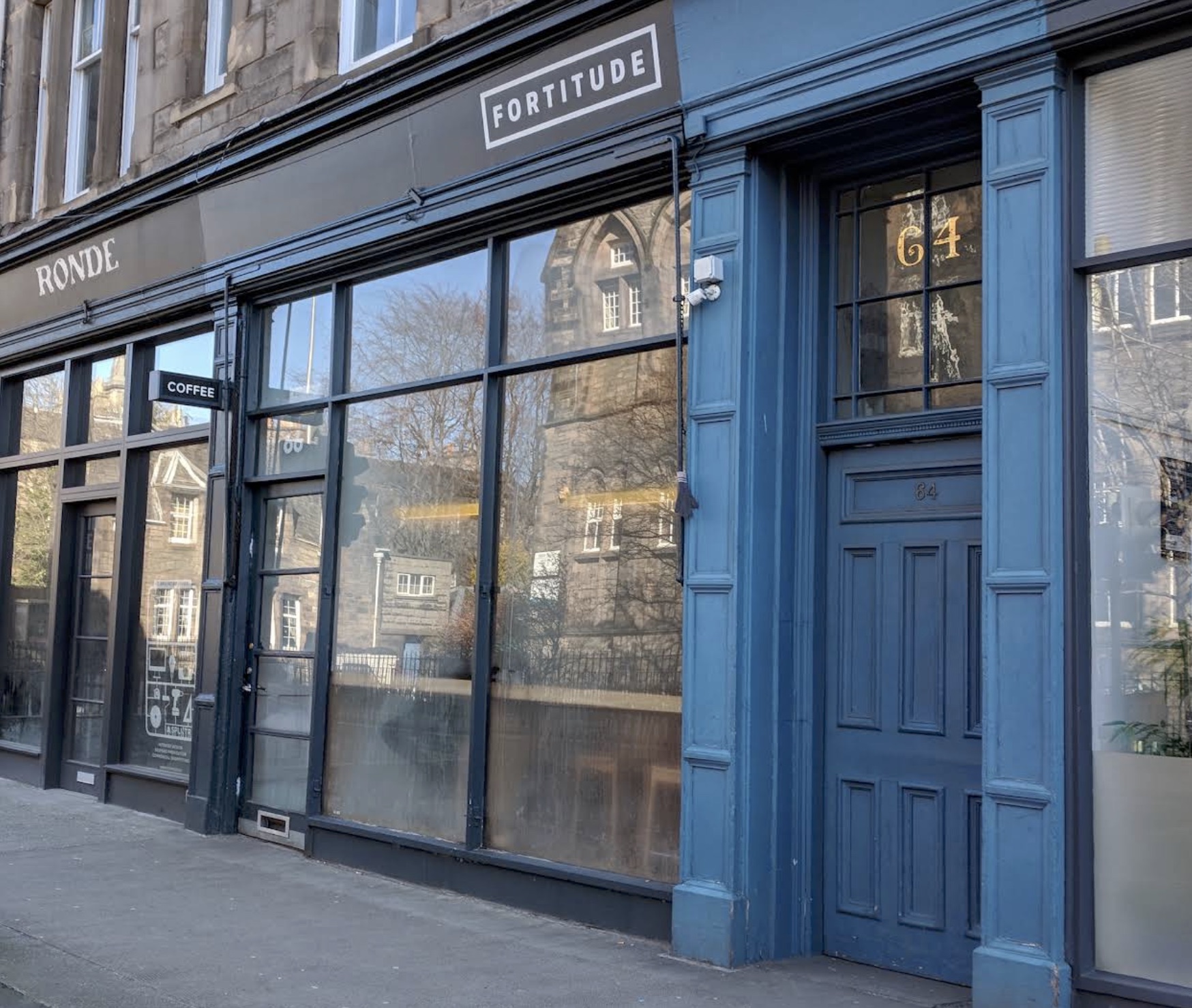 Fortitude Coffee's dark blue shopfront at number 64 with the white FORTITUDE sign above tall windows reflecting the stone tenements across the street