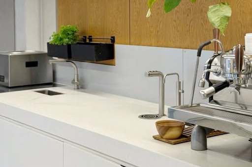 Lowdown's white marble counter with a chrome espresso machine, twin taps, and an oak shelf lined with cups and trailing greenery against a wood panelled wall