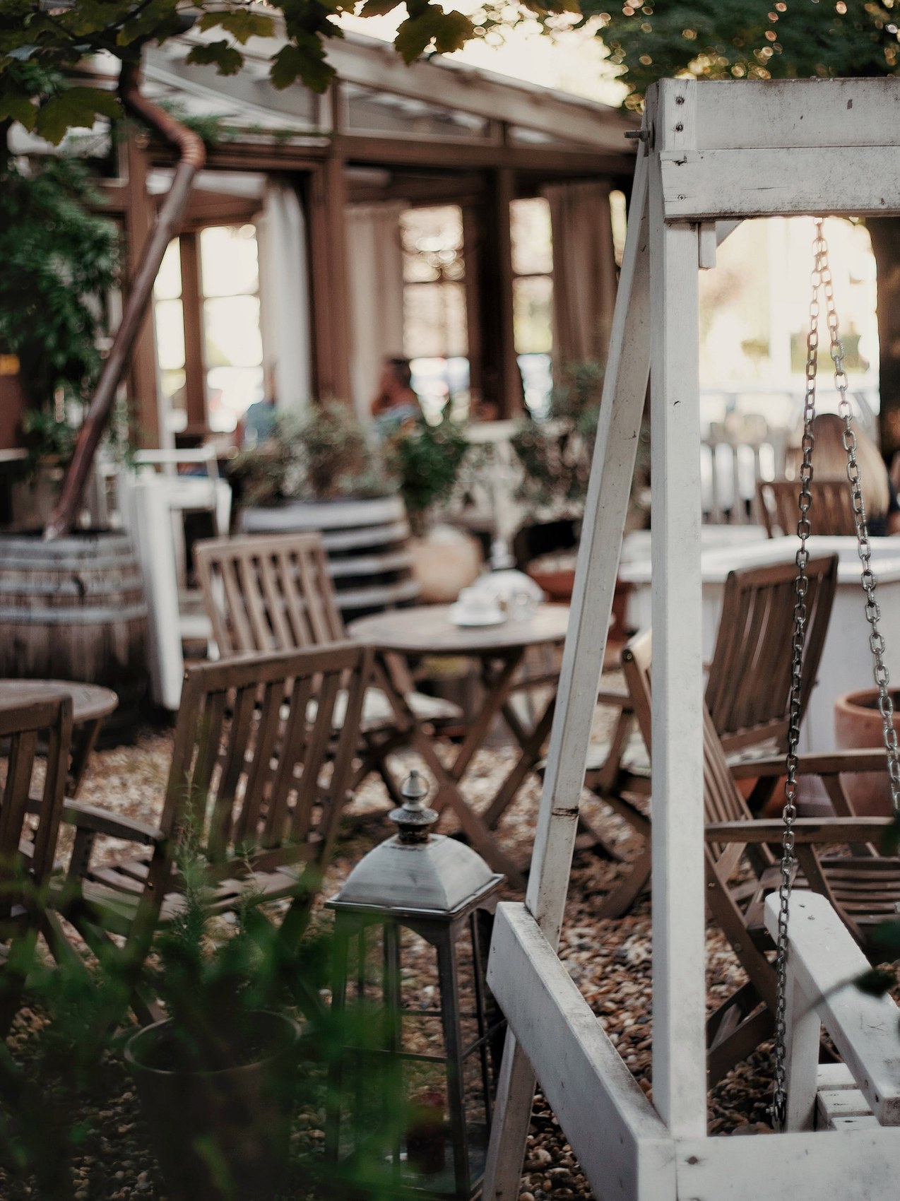 The garden patio at Kis Sziget Kávézó, with wooden folding chairs, a lantern, and a swing bench among potted plants