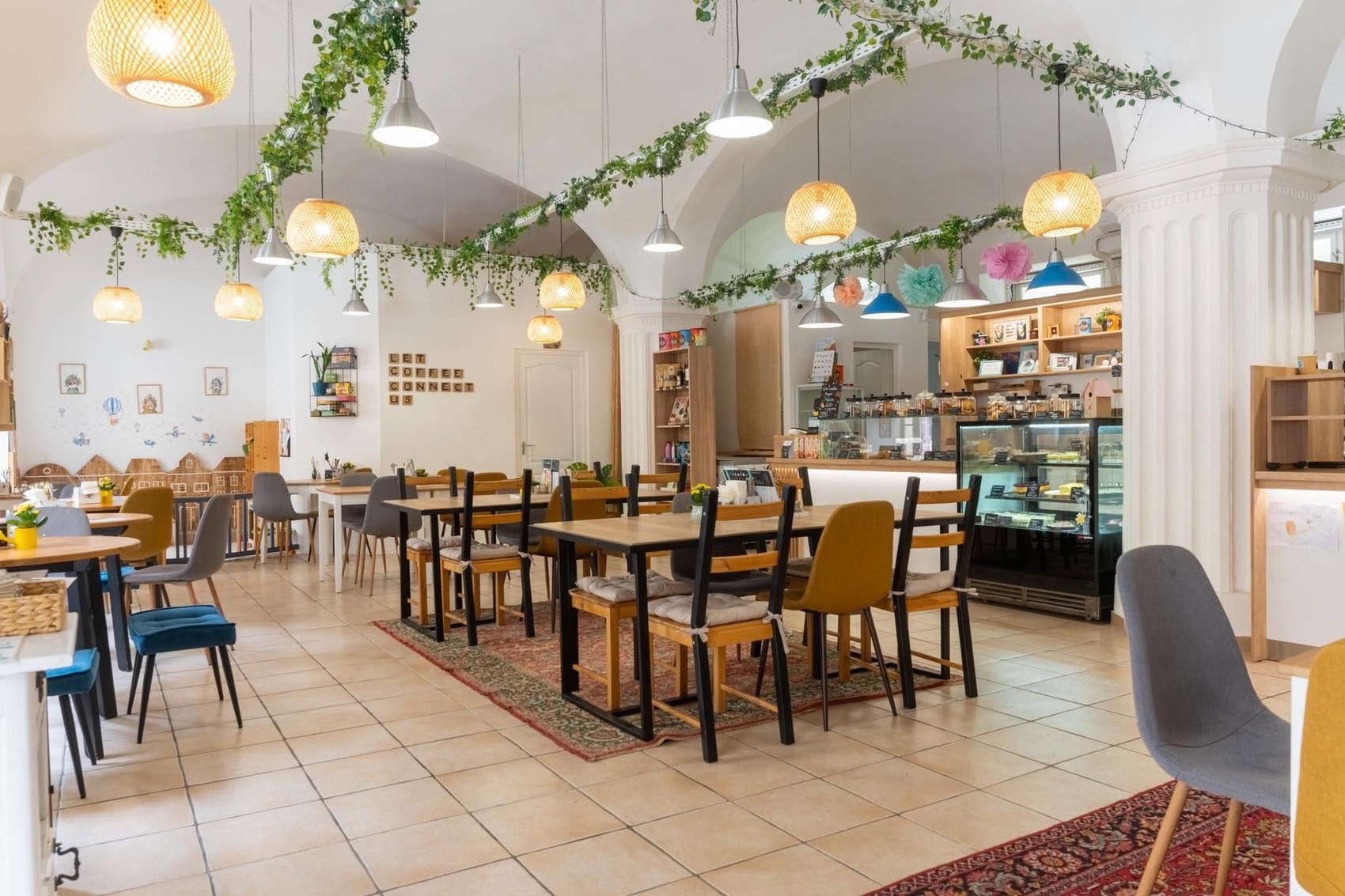 The vaulted dining room at Manooka Kávézó, with hanging plants, paper lantern lights, and a pastry counter