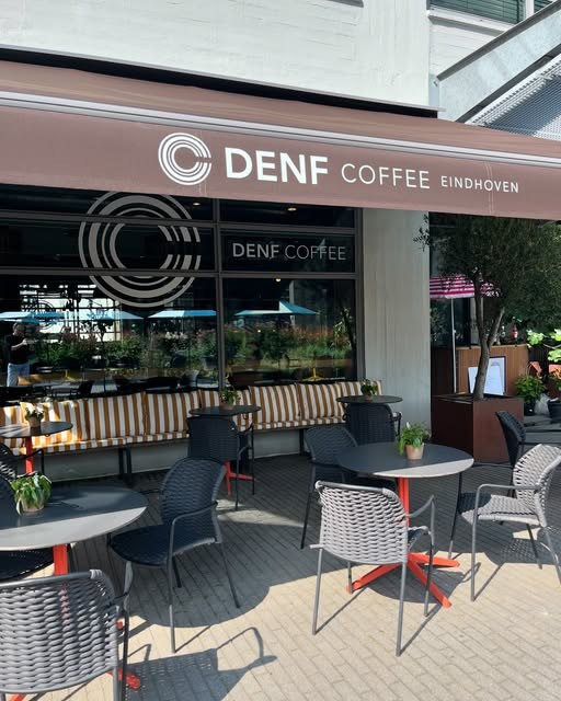 The storefront awning reading DENF COFFEE EINDHOVEN above an empty terrace of tables and chairs