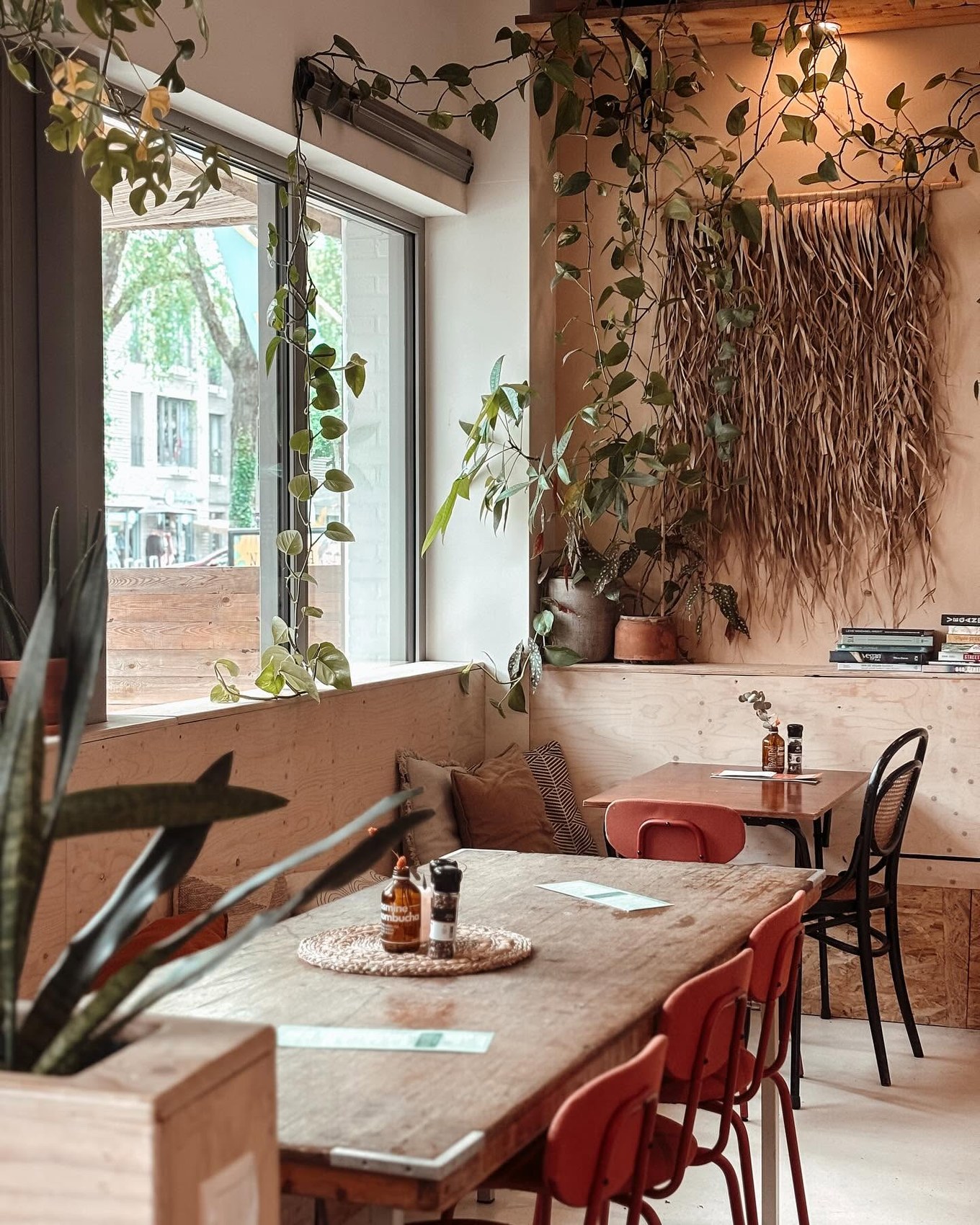 The plywood dining room hung with trailing vines and a dried grass wall panel, red bentwood chairs at a reclaimed wood table