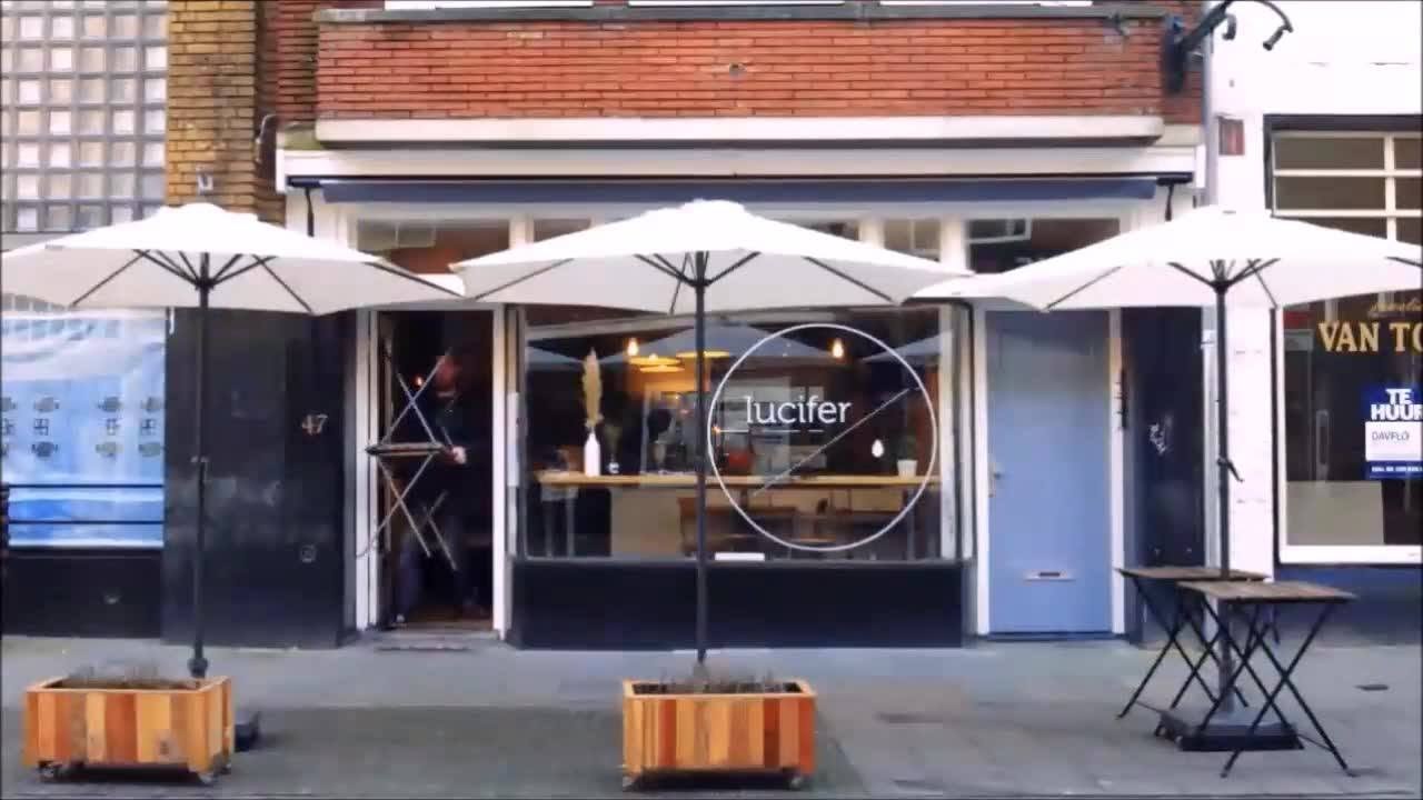 The Kleine Berg storefront with a circular lucifer logo etched on the window and white terrace umbrellas out front