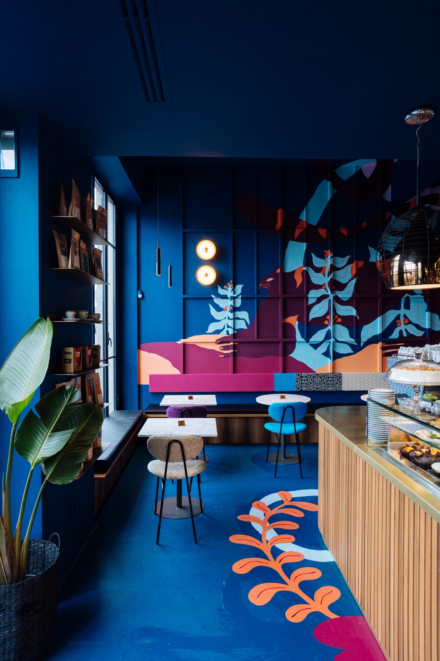 A colorful mural covered room at Ditta Artigianale with a deep blue wall, cafe tables, and retail bags on a shelf