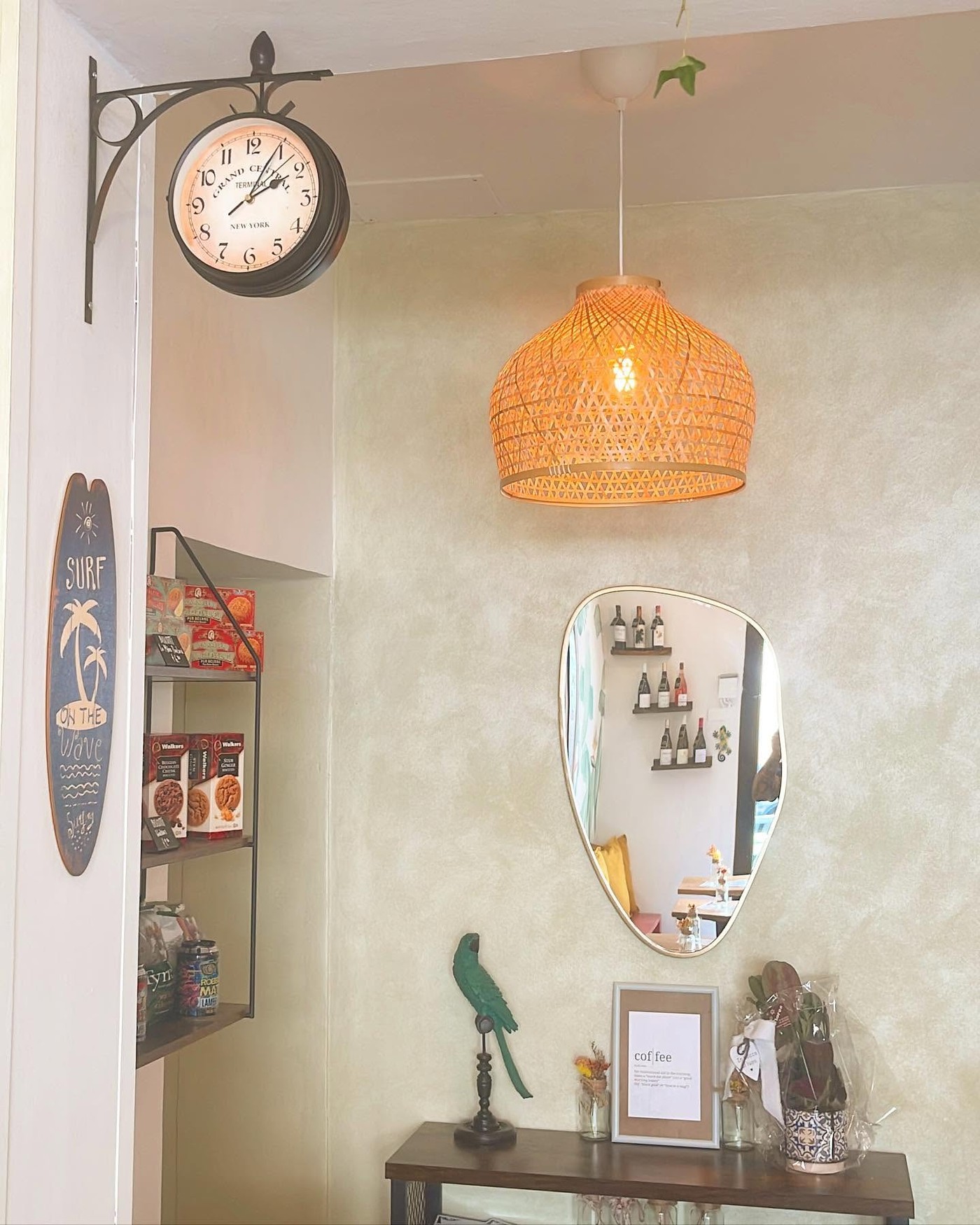 A corner of Manly The Office with a wicker pendant lamp, a vintage station clock, and a surf themed decor shelf