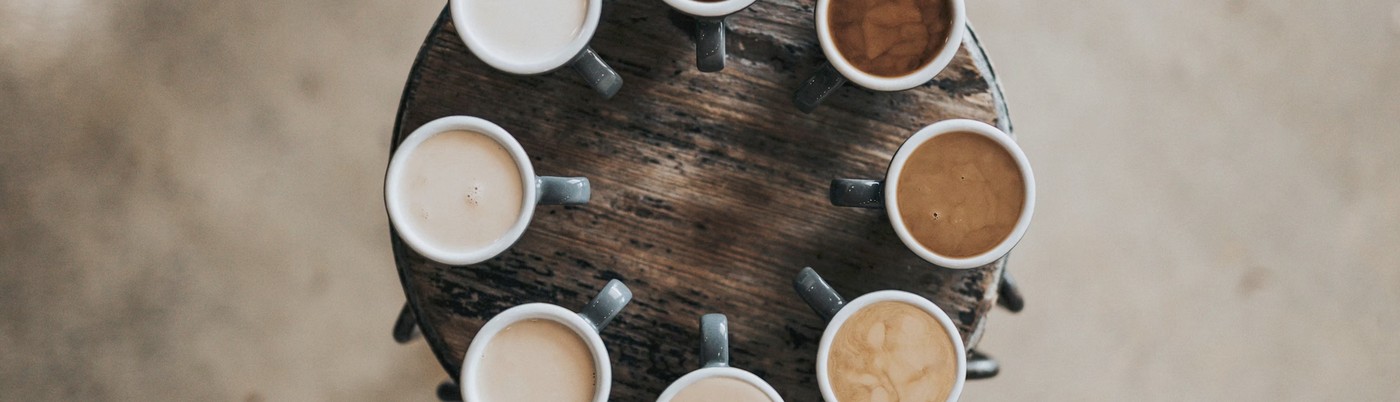 An overhead view of cups holding different coffee drinks arranged in a circle on a round wooden table