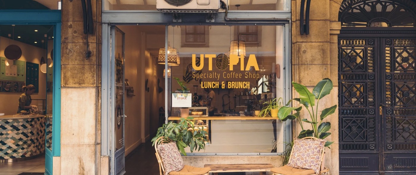 The Utopia storefront window with its Specialty Coffee Shop and Lunch and Brunch signage, plants framing the entrance
