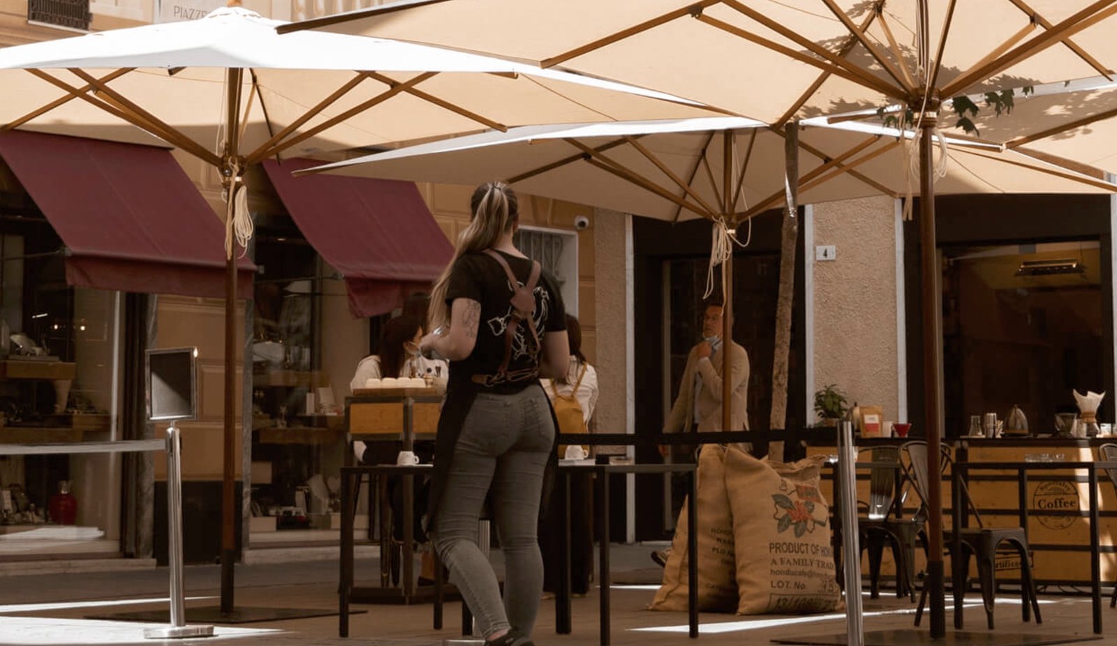 The terrace at Costadoro Social Coffee under umbrellas, with jute coffee sacks stacked beside the outdoor tables