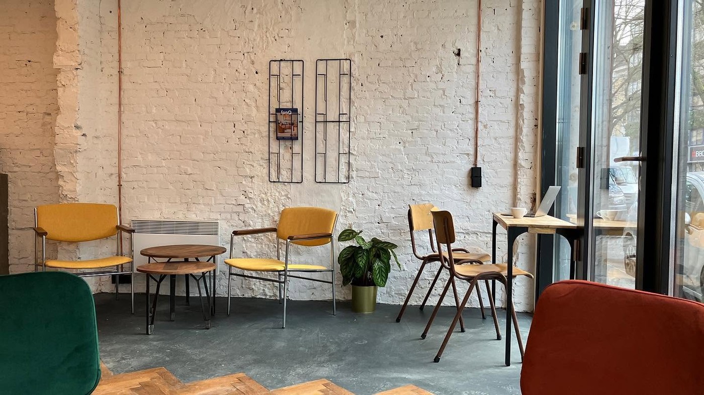 A seating nook at Full Circle Coffee with mustard yellow armchairs, wooden school chairs, and an exposed white brick wall
