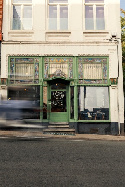 The green art nouveau facade of OR Coffee Lab, with the round OR Coffee Lab logo etched on the glass door