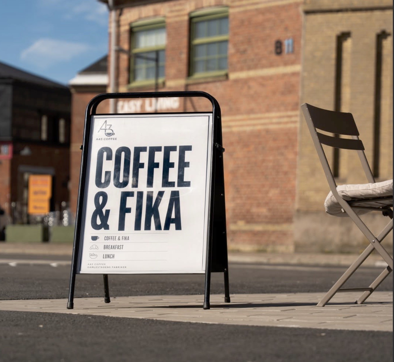 An A43 Coffee sandwich board advertising coffee, fika, breakfast, and lunch on a brick paved street